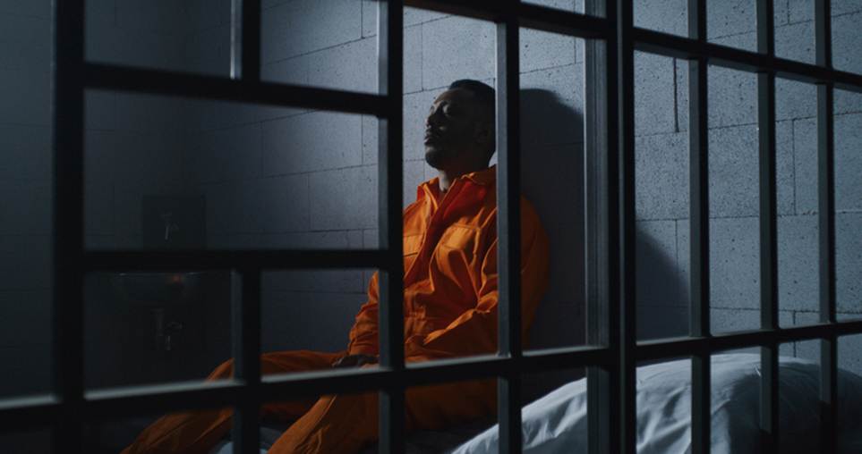 The image shows a person in an orange jumpsuit sitting in a jail cell. This somber image accompanies a legal text discussing the standards for detainment in New York.